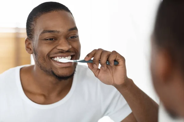 朝のルーティンコンセプト。バスルームでミラーの近くに幸せな黒人男性ブラッシング歯, — ストック写真