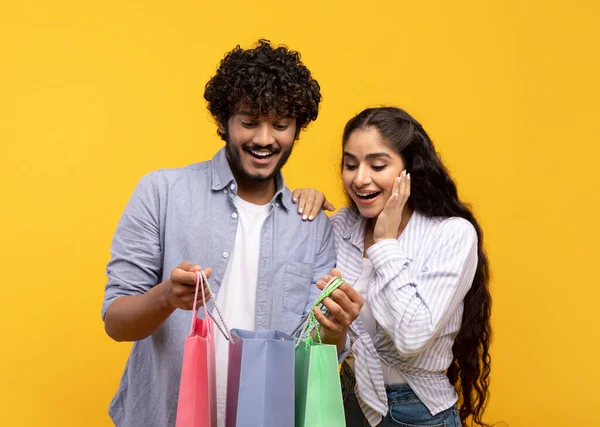 Comerciantes. Pareja india llena de alegría sosteniendo bolsas de compras, mirando dentro, emocionados por sus nuevas compras —  Fotos de Stock