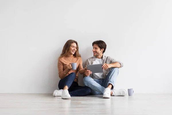 Усміхнені тисячоліття європейські чоловіки і жінки планують майбутній інтер'єр з планшетом, сидять на підлозі з кавою — стокове фото