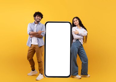 Genç Hintli eşler modelli akıllı telefonun yanında poz veriyorlar, mobil uygulama veya web sitesini tanıtıyorlar, boş alan