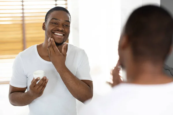 Aftershave Gondozás. Vonzó afro-amerikai srác használ hidratáló krém a fürdőszobában — Stock Fotó
