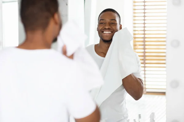 Higiene diaria. Hombre negro guapo limpiando la cara con toalla en el baño — Foto de Stock