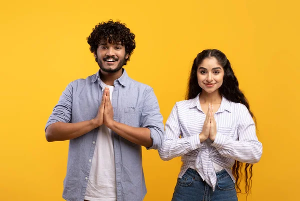 Couple indien paisible mettre les mains ensemble en namaste ou geste de prière, en regardant la caméra sur fond jaune — Photo