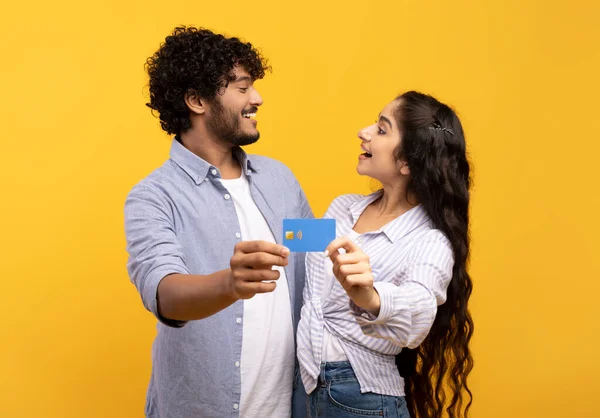 Cónyuges indios felices abrazándose, mostrando la tarjeta de crédito a la cámara y mirándose entre sí, recomendando el servicio bancario — Foto de Stock
