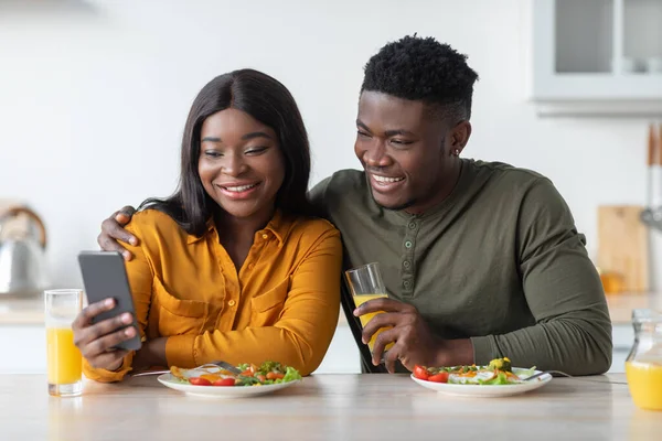 在厨房吃早餐的时候用智能手机快乐的黑人夫妇 — 图库照片