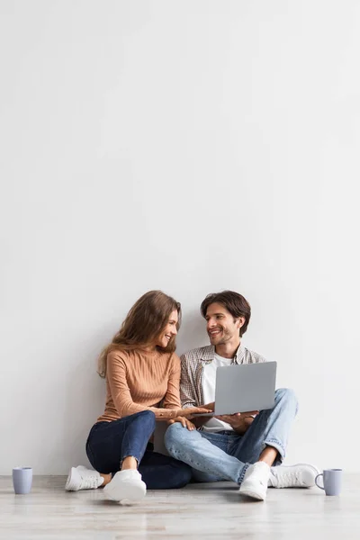 Glad ung kaukasier kille och kvinna planerar framtida interiör med laptop och sitta på golvet med kaffe — Stockfoto