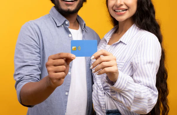 Cropped view of indian couple holding credit card on yellow studio background, focus on hands — Stock Photo, Image