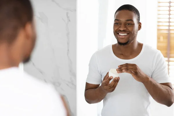 Hudvårdskoncept. Le ung svart man tillämpa närande grädde på ansiktet — Stockfoto