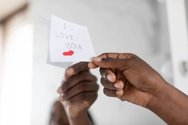 Preto feminino mão colocando pegajoso nota com amor mensagem no espelho, close-up — Fotografia de Stock