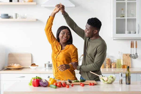 Retrato de alegre casal romântico preto dançando na cozinha enquanto cozinha — Fotografia de Stock