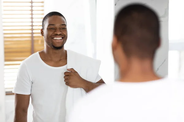 Schwarz schöner Mann mit Handtuch auf der Schulter Blick auf Spiegel im Badezimmer — Stockfoto