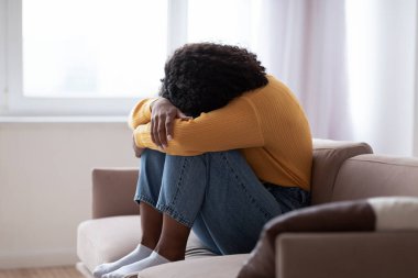 Depresyondaki genç siyah kadın evdeki kanepede ağlıyor.