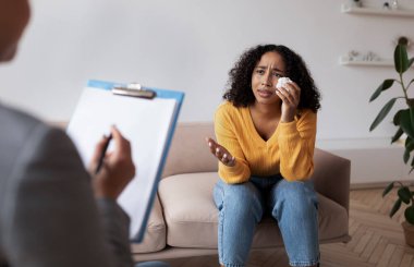 Genç Afrikalı Amerikalı kadın psikologla seansta ağlıyor, ofiste ruh sağlığı uzmanıyla konuşuyor.