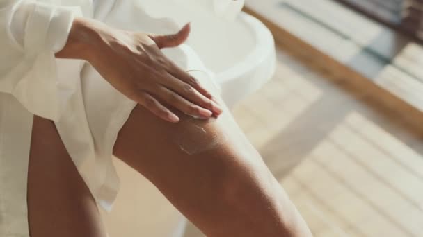 Cosméticos para el cuidado de la piel. Irreconocible dama afroamericana aplicando crema nutritiva en sus piernas, espacio libre — Vídeos de Stock