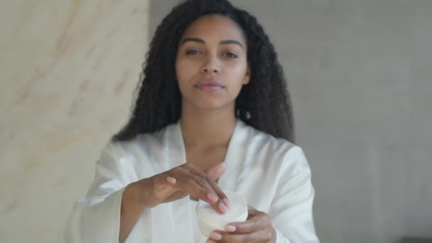 Procedimentos de beleza matinal. Jovem afro-americana tomando creme de mimos do frasco e aplicando-o no rosto, zoom in — Vídeo de Stock