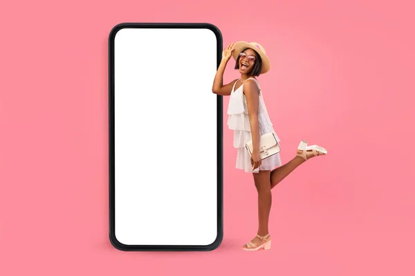 Cool mobile app. Black lady posing near big smartphone with blank screen, demonstrating space for your design or ad — Stock Photo, Image
