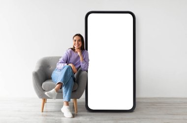 Boş ekranlı akıllı telefonun yanında oturan mutlu kadın, çevrimiçi hizmetler, uygulama veya web sitesi öneriyor