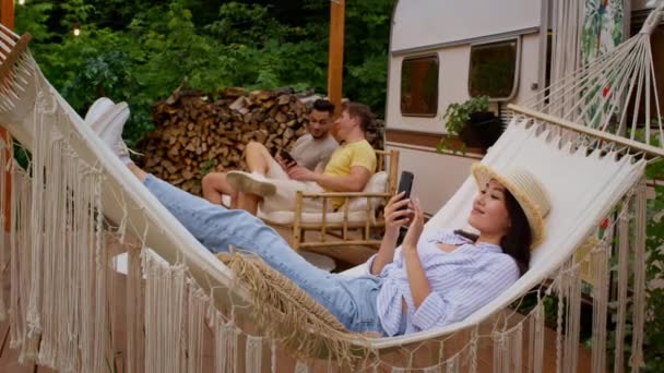 Молодая азиатка кемпинг с друзьями, расслабляясь со смартфоном в Hammock на открытом воздухе — стоковое видео
