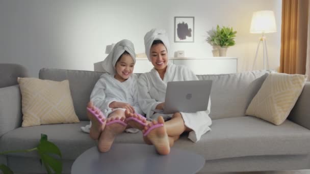 Kobiecość i zabawa. Zoom w portrecie szczęśliwej azjatyckiej matki i jej córki korzystających zabiegi spa w domu z laptopem — Wideo stockowe
