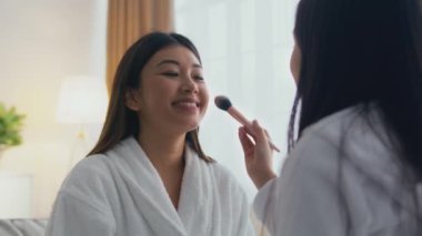 Evde spa günü. Küçük Asyalı kız, neşeli annesine makyaj yapıyor. Makyajdan hoşlanan kadınlar, zum yapıyor.