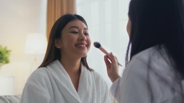 Día de spa en casa. Pequeña chica asiática aplicando maquillaje a su alegre madre, hembras disfrutando de maquillaje, zoom en tiro — Vídeos de Stock