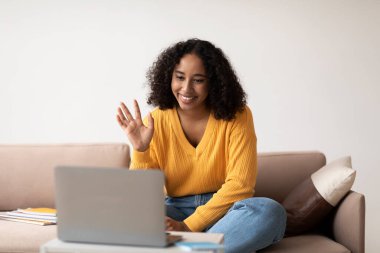 Afro-Amerikan bayan videosu dizüstü bilgisayardan arıyor, oturma odasındaki bilgisayar kamerasına el sallıyor. Milenyum siyahi kadın internet üzerinden iletişim kuruyor, evdeki modern aletleri kullanıyor.