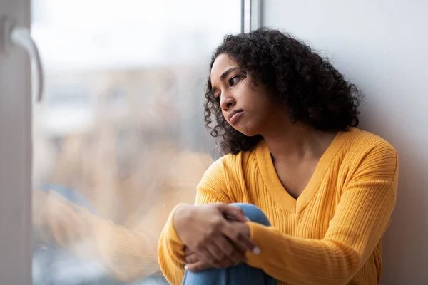 抑圧された若いアフリカ系アメリカ人の女性が窓の近くに座って 通りの外を見て 自宅で絶望的な感じ コピースペース 季節性気分障害精神疾患の概念 — ストック写真