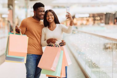 Eğleniyorum. Alışveriş merkezinden alışveriş yaptıktan sonra selfie çeken mutlu Afrikalı çift, alışveriş torbalarıyla ayakta duruyor, kameraya gülümsüyor, elinde akıllı telefonlara bakıyor, bedava fotokopi çekiyor.