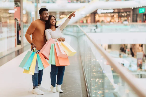 Mutlu Müşteri Konsepti. Gülümseyen Afro-Amerikan bir çift alışveriş merkezinde yürüyor, vitrine bakıyor, kadın butik pencereyi işaret ediyor, bedava fotokopi çekiyor. Mevsimlik Satış ve Özel Teklif