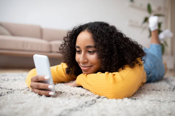 Молодая Чернокожая Дама Лежит Полу Мобильным Телефоном Проверяет Социальные Сети — стоковое фото