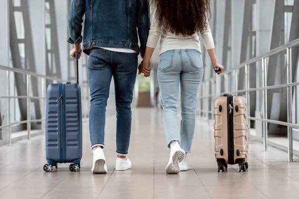 Pareja joven irreconocible caminando en el aeropuerto con maletas, vista trasera — Foto de Stock