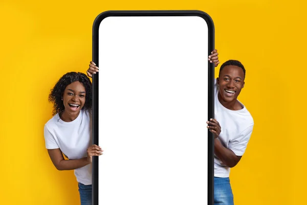 Happy african american man and woman posing near big cellphone with blank white screen, mockup — Stock Photo, Image