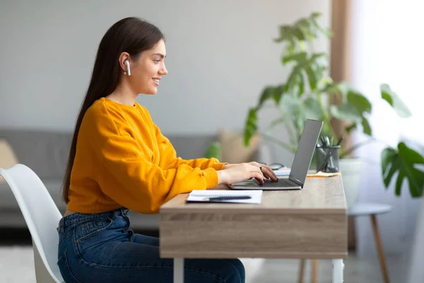 Joven mujer alegre en auriculares usando el ordenador portátil, teniendo reunión de negocios en línea o seminario web educativo en casa — Foto de Stock