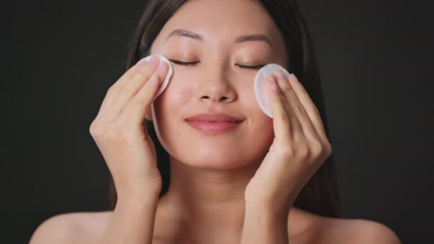 Makyaj temizliği. Genç, güzel Asyalı kadın yüzünü pamuk pedlerle ve mikiler suyuyla temizliyor. Makyajını temizliyor. — Stok video