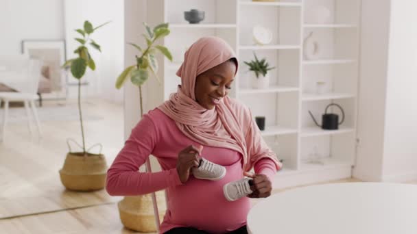 Embarazada africana mujer usando pañuelo para la cabeza jugando con zapatos de bebé en interiores — Vídeos de Stock