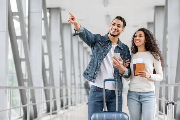 Heureux couple arabe avec smartphone debout à l'aéroport et pointant loin — Photo