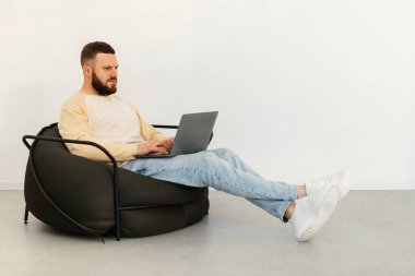 Bilgisayarı kullanan adam çevrimiçi çalışıyor. İçeride Sandalyede oturuyor.