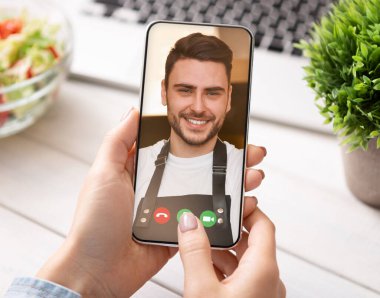 Mutfakta yemek pişirirken yakışıklı aşçıyla video görüşmesi yapan tanınmayan bir kadın.