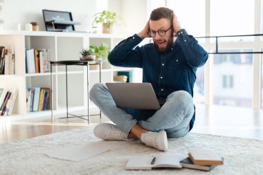 Şok olmuş adam dizüstü bilgisayara bakıyor. İçerde oturmuş bağırıyor.