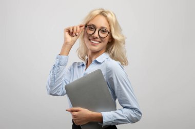 Başarılı genç iş kadını elinde dizüstü bilgisayar, gözlükleriyle kameraya gülümsüyor.