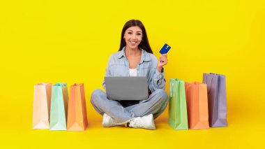 Alışveriş torbaları, dizüstü bilgisayarı ve plastik kartı olan mutlu bir kadın.