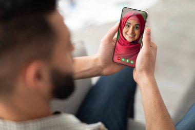 Arap adam, akıllı telefonda modern uygulamayı karısıyla görüntülü konuşma yapmak için kullanıyor.