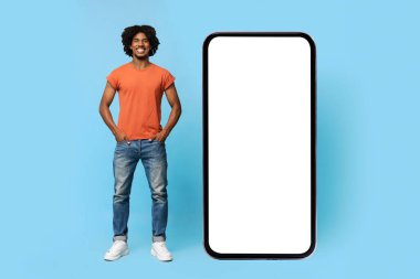 Havalı siyahi adam kocaman bir cep telefonunun yanında duruyor.
