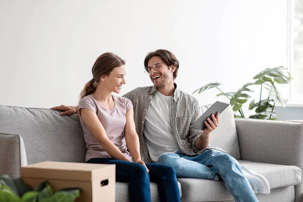 Feliz jovem caucasiano marido feliz em óculos e esposa em casual relaxante no sofá com tablet, planejando novo interior — Fotografia de Stock