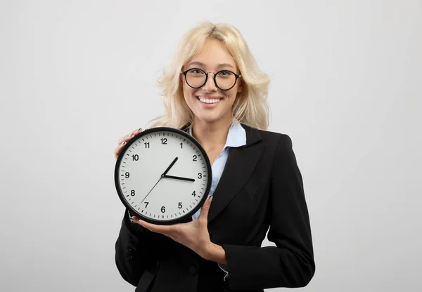 Zeitmanagement und Optimierungskonzept. Glückliche junge Geschäftsfrau hält Uhr, hellgrauer Studiohintergrund — Stockfoto