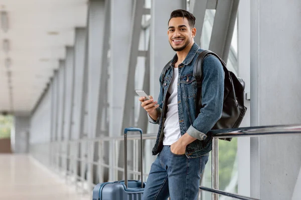 Porträt eines fröhlichen jungen Arabers, der am Flughafen auf sein Smartphone wartet — Stockfoto