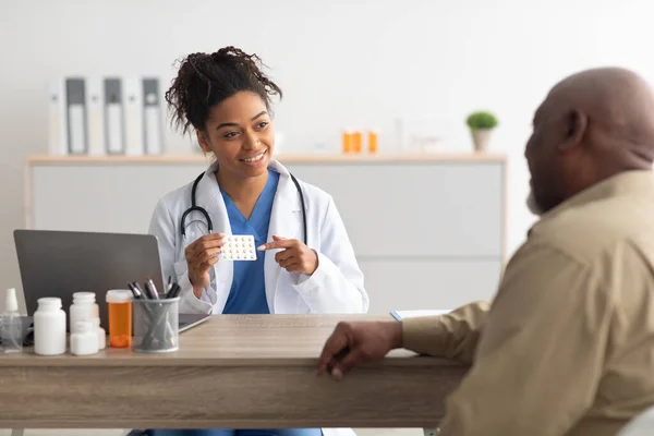 Médico preto experiente mostrando pílulas para paciente do sexo masculino — Fotografia de Stock