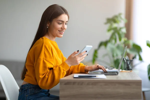 Jovem alegre usando laptop e celular para trabalho à distância, comunicando on-line a partir de casa, espaço livre — Fotografia de Stock