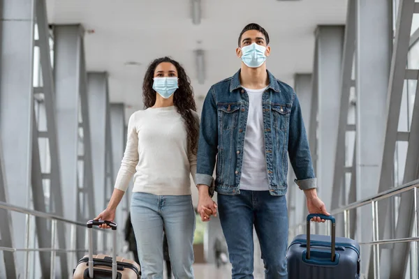 Viajes pandémicos. Cónyuges de Oriente Medio con máscaras faciales médicas caminando en el aeropuerto —  Fotos de Stock