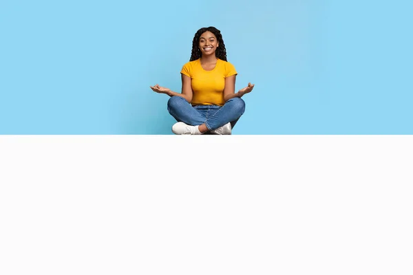 Positive african american lady meditating on empty board — Stock Photo, Image